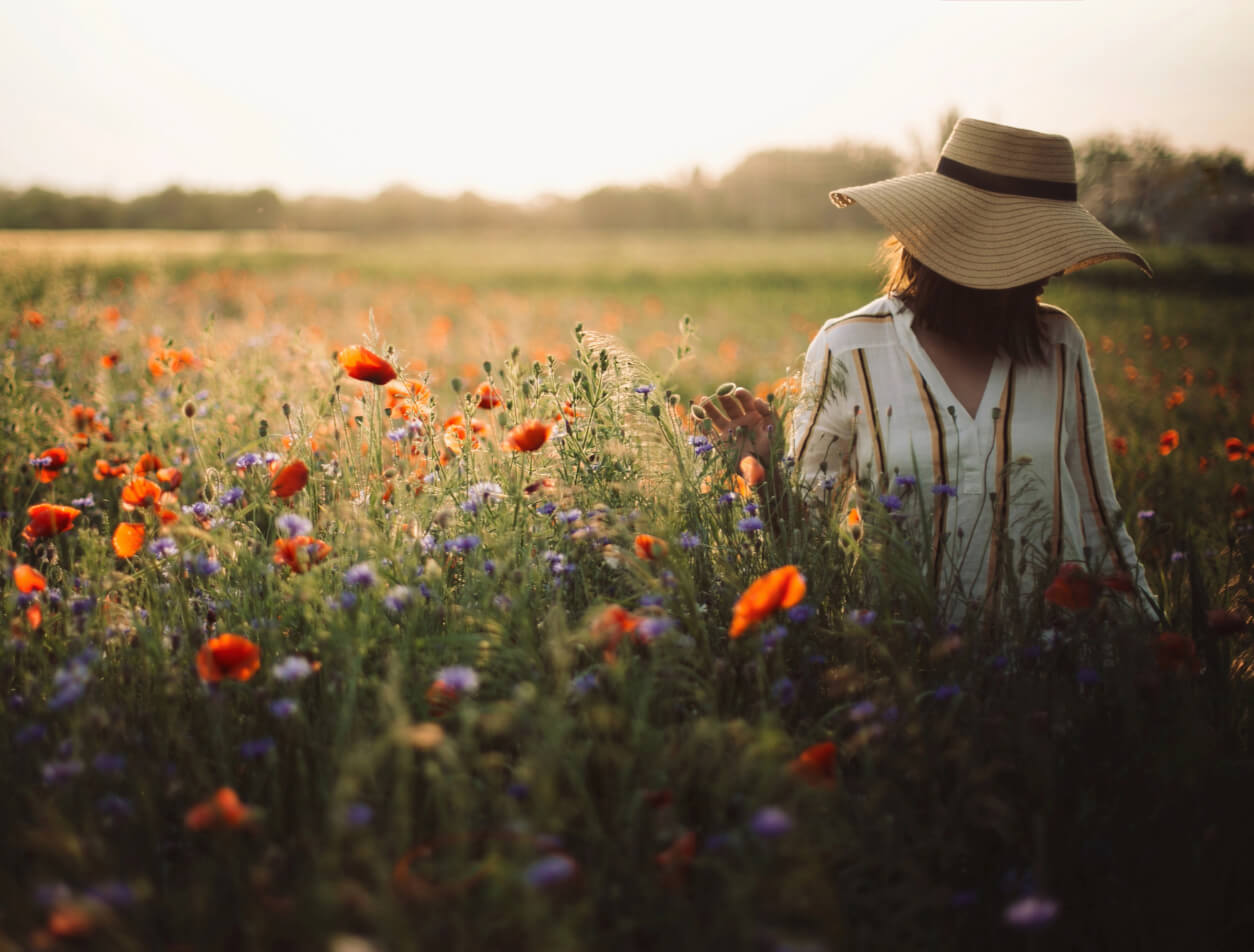 Frau mit Hut steht bei Sonnenuntergang auf einer sommerlichen Wiese